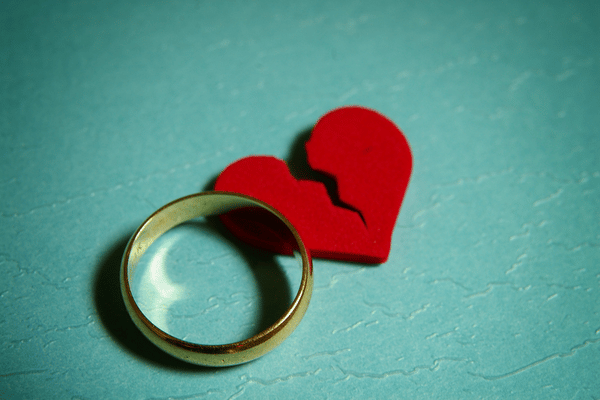 man's gold wedding band laying next to a red broken heart