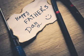 Burnt piece of paper with sharpie writing that says "Happy Father's Day" with a smiley face drawn next to it and tools laying on either side of the message