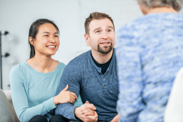 A female and male couple sitting together smiling with a mediator working together with the mediator to discuss where they see their future ending up and what steps they need to take to make that happen.