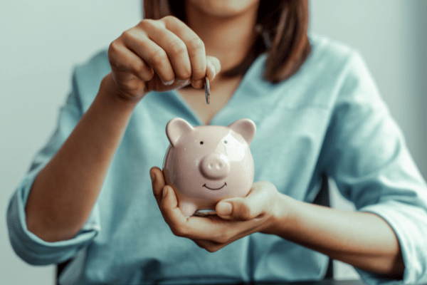 lady holding a smiling piggy bank putting a coin into it to save money