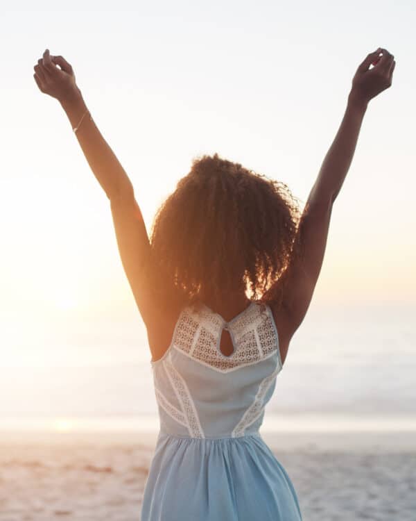Happy woman on the beach during sunset with her arms outstretched represending the joy associated with a successful mediation