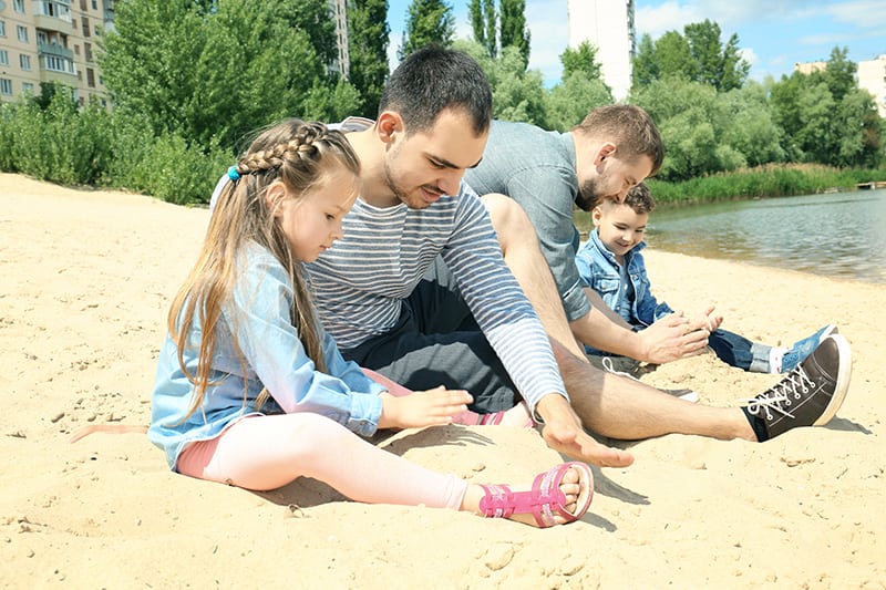 Male gay couple with children playing in sand